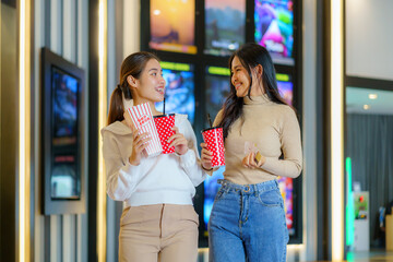 Asian friends walk in front of the cinema holding glasses and popcorn having fun.