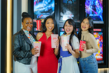 A group of multiethnic friends walk in front of the cinema holding glasses and popcorn having fun.