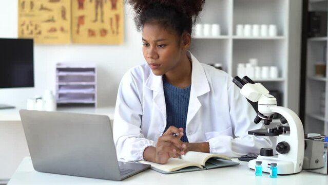 Female medicine doctor, physician or practitioner in lab room writing on blank notebook and work on laptop computer, analysis the blood test examination results and medication usage.