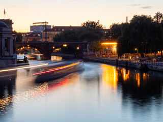 View of the city river at dusk. Light trails on the river from passing boats.