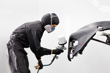 Car painting service worker in protective suit varnishing automobile bumper. Male auto painter...