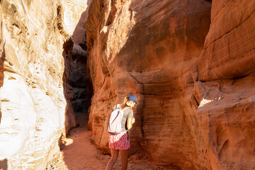 Woman walking in the narrow Kaolin Wash slot canyon along White Domes Hiking Trail in Valley of Fire State Park in Mojave desert, Nevada, USA. Massive cliffs of striated red and white rock formations