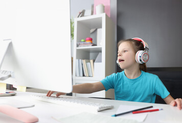Obraz na płótnie Canvas Little girl in headphones is engaged in training remotely. Kids online games concept
