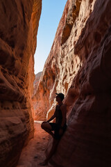 Man walking in the narrow Kaolin Wash slot canyon along White Domes Hiking Trail in Valley of Fire State Park in Mojave desert, Nevada, USA. Massive cliffs of striated red and white rock formations