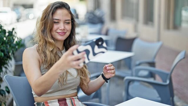 Young beautiful hispanic woman making selfie by the smartphone sitting on table smiling at coffee shop terrace