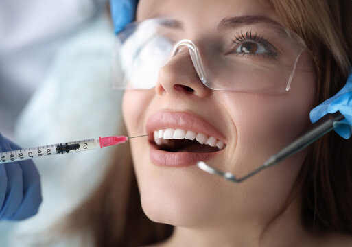 Portrait of young female patient sitting in dentist chair with mouth open and receiving an injection of anesthetic. Painless dental treatment concept
