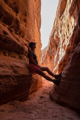 Woman climbing the walls in narrow Kaolin Wash slot canyon on White Domes Hiking Trail in Valley of Fire State Park in Mojave desert, Nevada, USA. Massive cliffs of striated red white rock formations