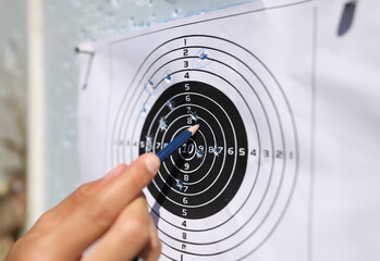 Man showing with pencil to shots on paper target closeup. Weapon shooting training concept