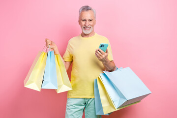 Photo of clever senior man with beard dressed yellow t-shirt hold new clothes make order in smartphone isolated on pink color background