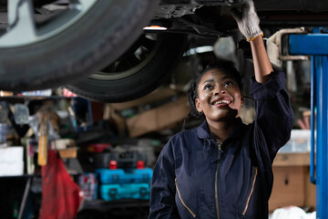 Obraz na płótnie Canvas African female mechanic checking and fixing underneath car in automobile repair shop