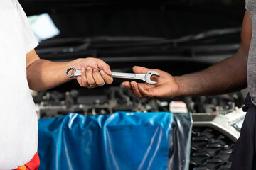 closeup mechanic hands giving wrench to coworker for fixing a car in automobile repair shop