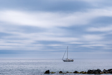 calm: sailboat on the horizon off a breakwater on a windless overcast day big sky room for text...