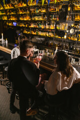 Obraz na płótnie Canvas Guys and girls enjoy fun with cocktails near bar in club. Relax in atmospheric nightclub with variety of alcoholic drinks