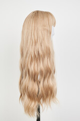 Naklejka premium Natural looking blonde wig on white mannequin head. Long hair on the plastic wig holder isolated on white background, side view.