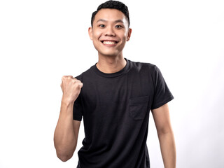 A portrait of an Asian man wearing a black t-shirt, looking joyful with a pose of raising his hands in victory, isolated on a white background.