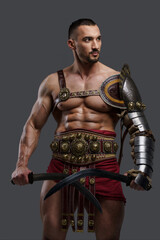 Elegant gladiator in stylish light armor holds two gladii in hands while striking a pose against a gray backdrop