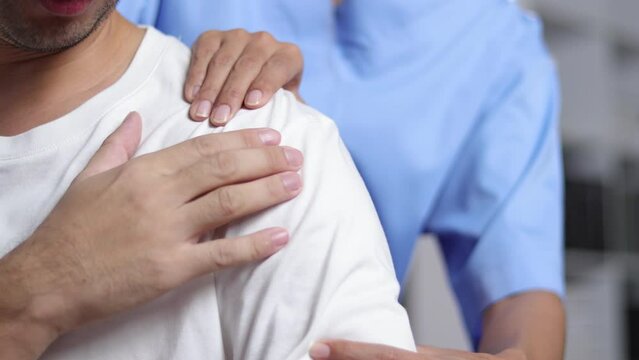 Doctor diagnosing man's shoulder pain in hospital examination room. Nurse doing massage and physiotherapy to treat patient's shoulder.