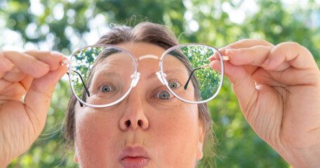 close up female face, funny woman in glasses with metal frame looks through lenses in surprise,...