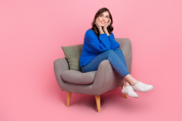 Full length portrait of adorable minded person sit cozy soft chair hands touch cheeks look empty space isolated on pink color background