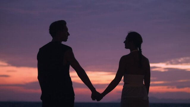 Silhouette romantic couple, a man takes a woman by the hand against the background of a sunset. Romantic couple at sunset against the backdrop of the sea in the evening. The concept of romantic date