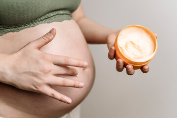 A pregnant woman uses a cream for stretch marks. Prevention of stretch marks on the abdomen and legs, skin care during pregnancy - obrazy, fototapety, plakaty
