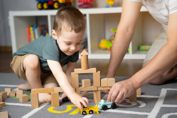 Little toddler boy 2,5 years playing wooden blocks and toy cars with dad. Spending time with children. Educational activities for kids. Children's room. Indoors