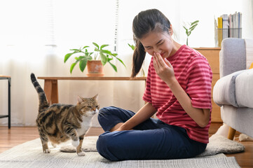 Young Asian woman sneezing which suffering from first symptoms of cat's fur allergy. Cute cat and allergic girl. Animal allergy people health illness concept.