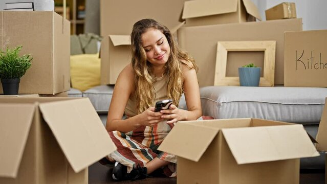 Young beautiful hispanic woman using smartphone sitting on floor at new home