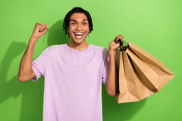 Portrait of cheerful satisfied person hold store shop bags raise fist success isolated on green color background