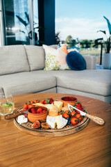 Cheeses, fruit and vegetables on a wooden cutting board in modern apartment