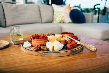 Cheeses, fruit and vegetables on a wooden cutting board in modern apartment