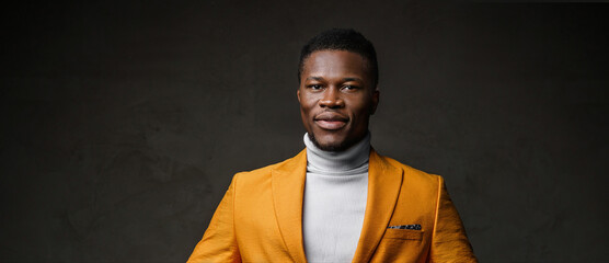 Portrait of a smartly dressed black man in a yellow blazer with short hair against a dark backdrop