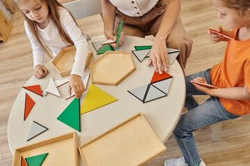high angle view of teacher and kids playing with triangles on table in montessori school