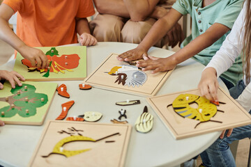 cropped view of interracial kids playing with didactic materials near teacher in montessori school - obrazy, fototapety, plakaty