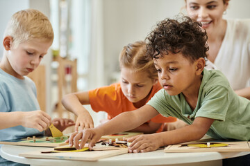 african american kid playing with didactic material near children and teacher in montessori school