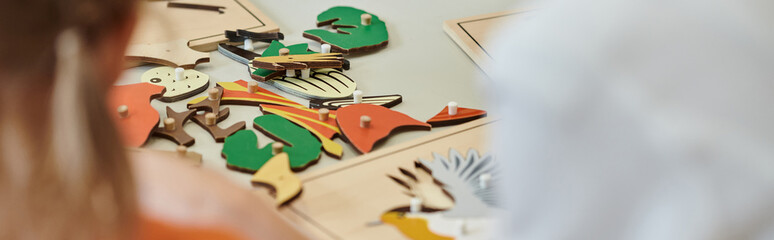 cropped view of didactic materials on table near blurred kids in montessori school, banner - obrazy, fototapety, plakaty