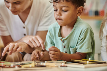focused african american kid playing near teacher during lesson in montessori school