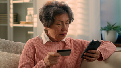Caucasian old woman senior granny elderly female mature lady retired grandmother with mobile phone and bank credit card paying online shopping with smartphone buying internet payment cellphone at home