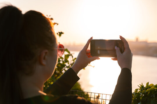 Girl taking photo other phone of Plymouth harbour at sunset