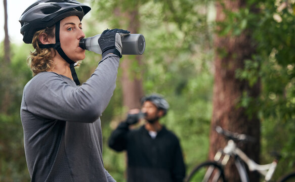 Forest, cyclist and men drinking water, exercise and tired with workout, refreshing and fitness. Healthy people, athlete and bikers in the woods, hydration and outdoor with liquid, bottles and helmet