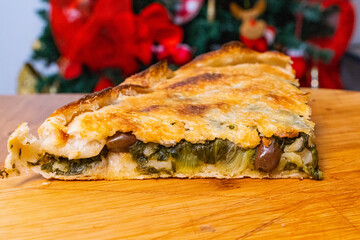 Pizza ripiena di scarole, acciughe, olive e mozzarella fotografata su un tagliere di legno con...