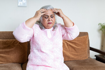 Tired, depressed senior woman sitting on couch in living room feeling hurt and lonely. Aged,...