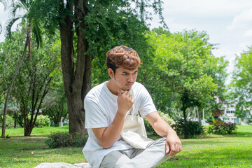 Portrait of an Asian man in a white t-shirt sitting on a rock, stressed out by problems going through life. tension concept