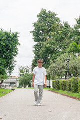 Fototapeta na wymiar A young man wearing a white T-shirt takes a relaxing walk in the park. urban relaxation concept