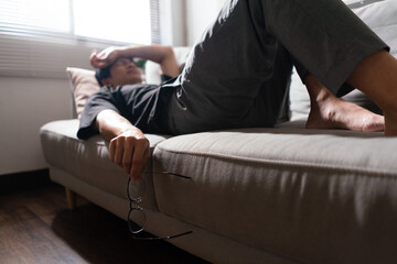 Man with mental health problem lying on couch and using arm to covering eyes with depressed emotion