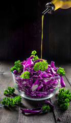 Cook pours olive oil into red cabbage salad