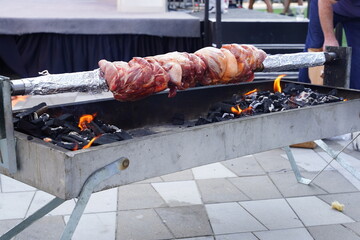 Pork meat is being grilled outside on a rotisserie grill.