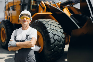 Happy Industrial worker male senior in helmet on background of production of excavator, working on...