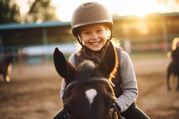 Tuinposter Happy girl kid at equitation lesson looking at camera while riding a horse, wearing horseriding helmet © Keitma