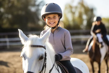 Foto op Plexiglas Happy girl kid at equitation lesson looking at camera while riding a horse, wearing horseriding helmet © Keitma